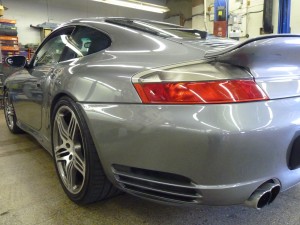 A silver car parked in a garage with its rear end.