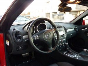 A car is shown with the steering wheel and dashboard.