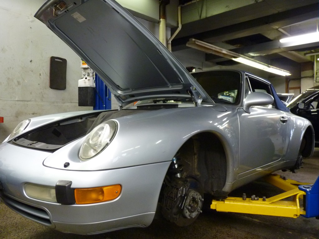 A silver car is being worked on by a mechanic.