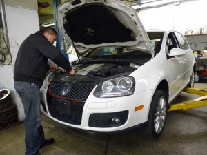 A man is working on the hood of a white Volkswagen.