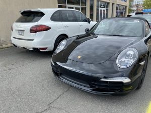 A black porsche parked in front of another white car.